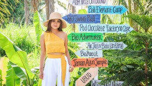 A person standing in front of a signpost with various destinations listed, surrounded by lush greenery. - Puri Lumbung Village (Carangsari)