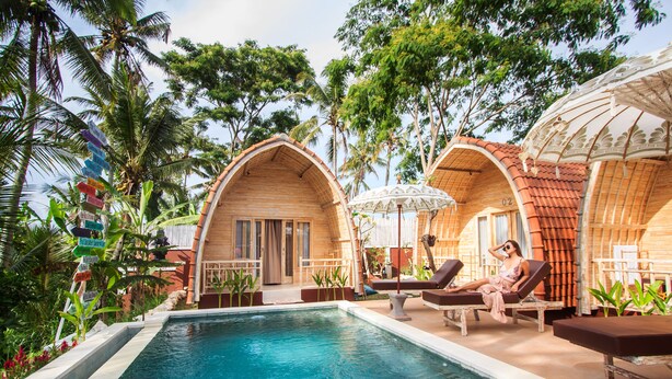 A pool area with lounge chairs, wooden arched structures, and tropical vegetation. - Puri Lumbung Village (Carangsari)