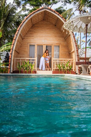 A wooden villa with a pool, featuring a balcony with a railing and a small garden area. - Puri Lumbung Village (Carangsari)