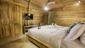 A wooden room with a bed, a desk, a television, and a mirror. - Puri Lumbung Village (Carangsari)