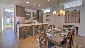 A modern kitchen with dark cabinetry, a central island with bar stools, and a dining area with a large table and chairs. - 068332: 'Desert Pearl' 3 BR Oasis w/ Private Pool! (La Quinta)