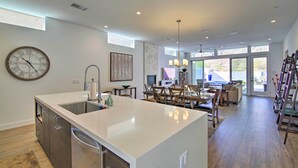 A modern kitchen with a large island, a dining area with a chandelier, and a view through large windows. - 068332: 'Desert Pearl' 3 BR Oasis w/ Private Pool! (La Quinta)