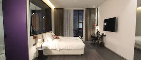 A modern hotel room with a large bed, a desk, and a TV.