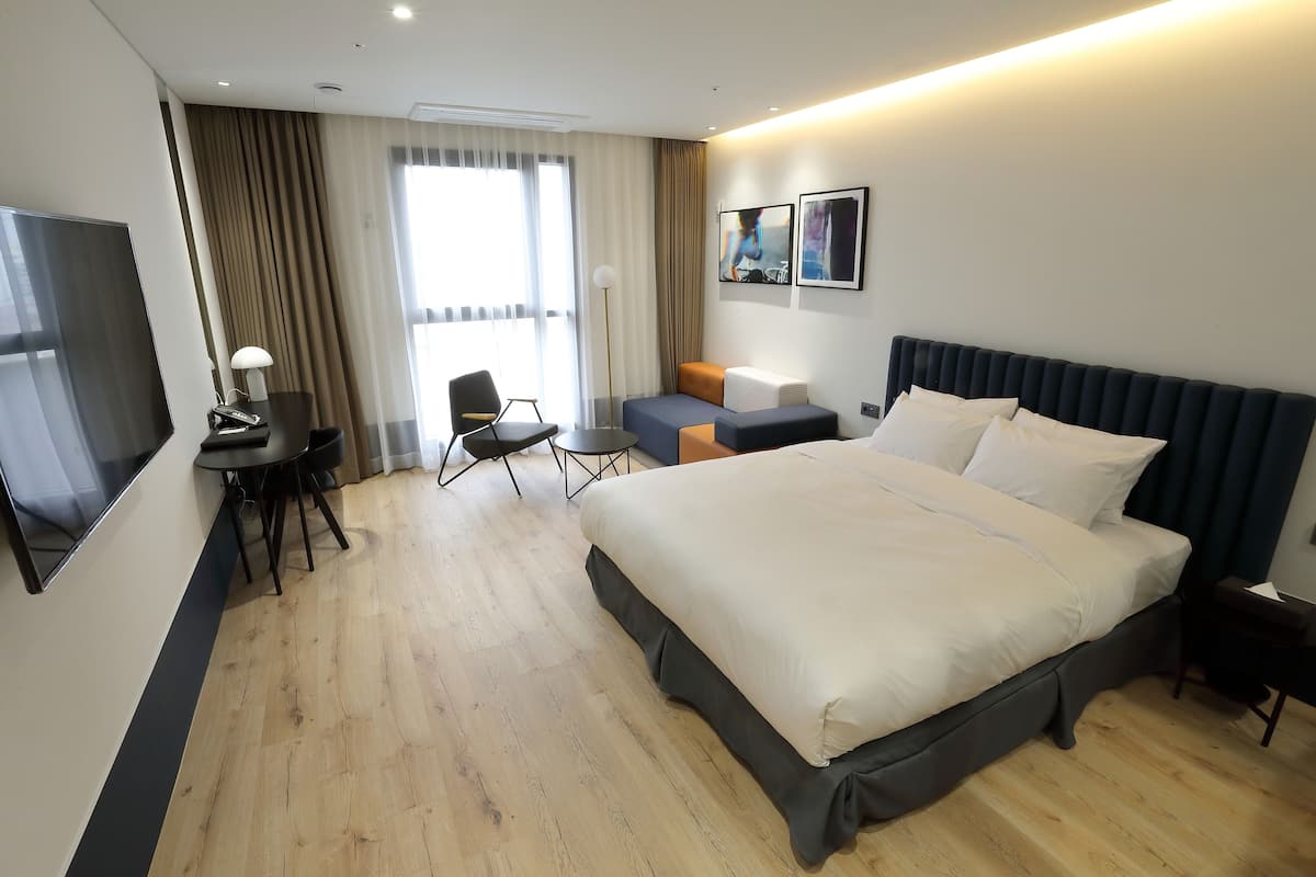 A hotel room with a large bed, a desk with a chair, a TV, and a view of the outdoors through the window.