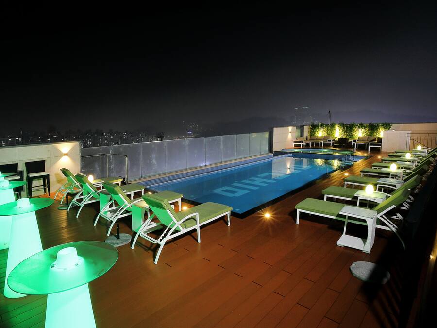 A rooftop pool area with lounge chairs and tables, surrounded by a glass railing.