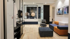 Een moderne woonkamer met een bank, een voetenbankje en een glazen scheidingswand met uitzicht op een keuken.