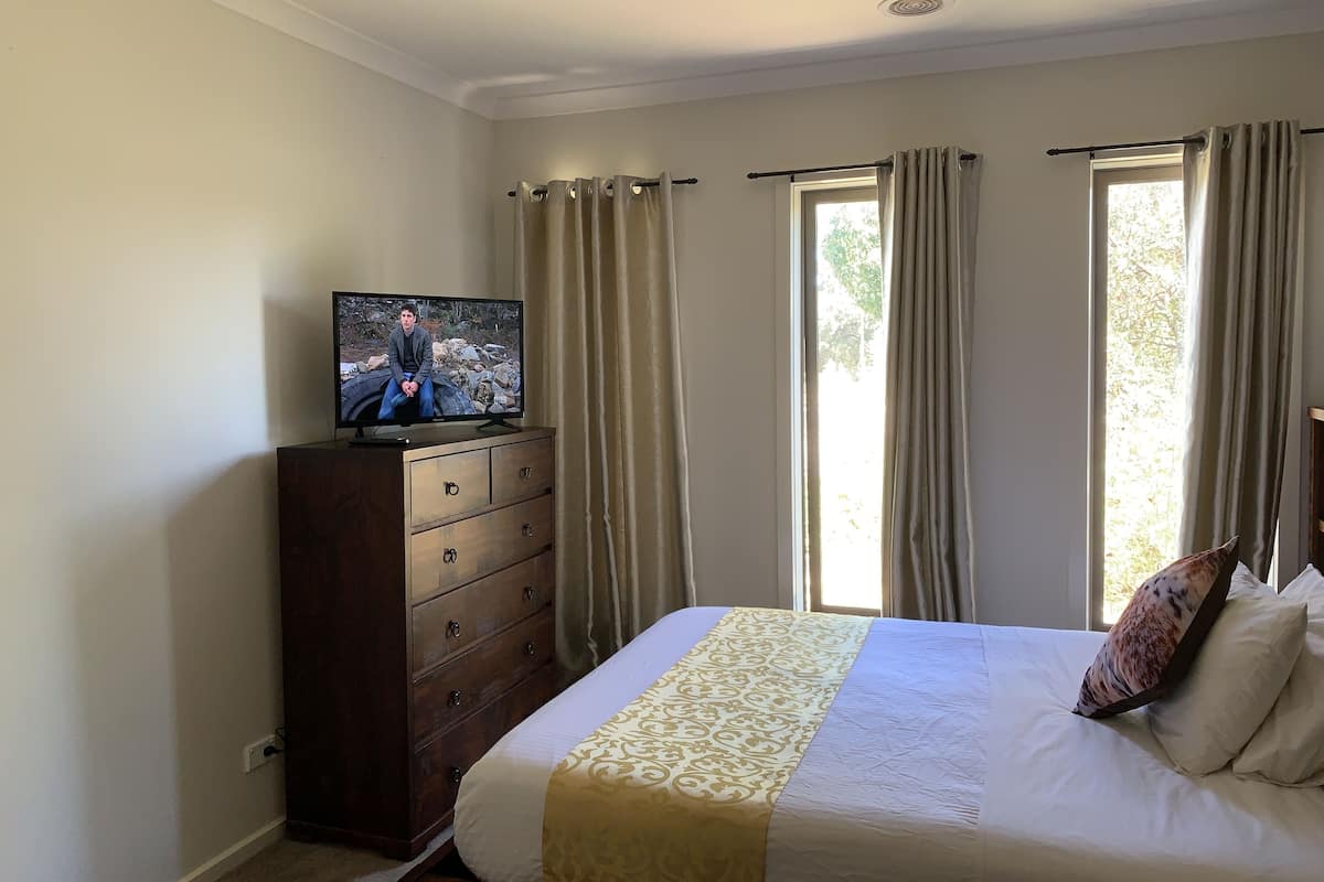 Une chambre à coucher avec un lit, une commode, un téléviseur posé sur la commode et une fenêtre avec des rideaux.