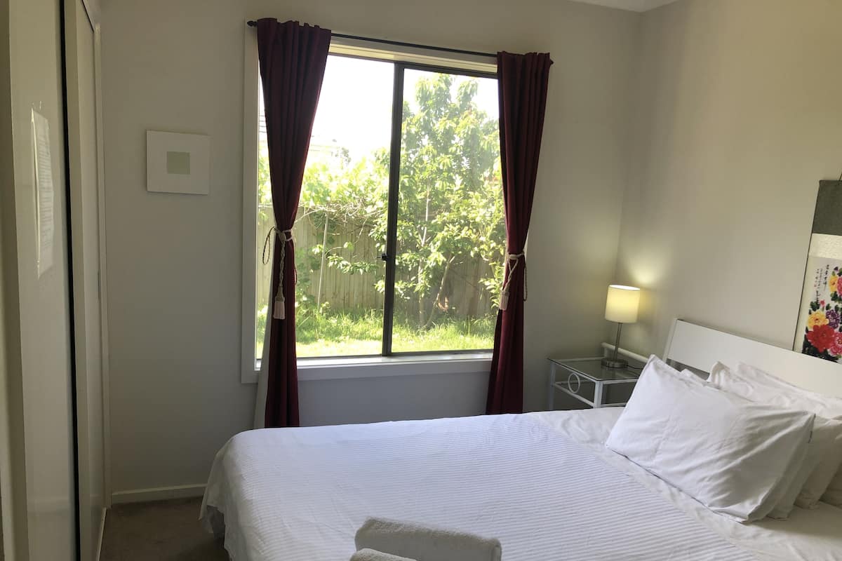 Une chambre d’hôtel avec un grand lit, du linge de lit blanc, une table de chevet avec une lampe et une fenêtre avec des rideaux.