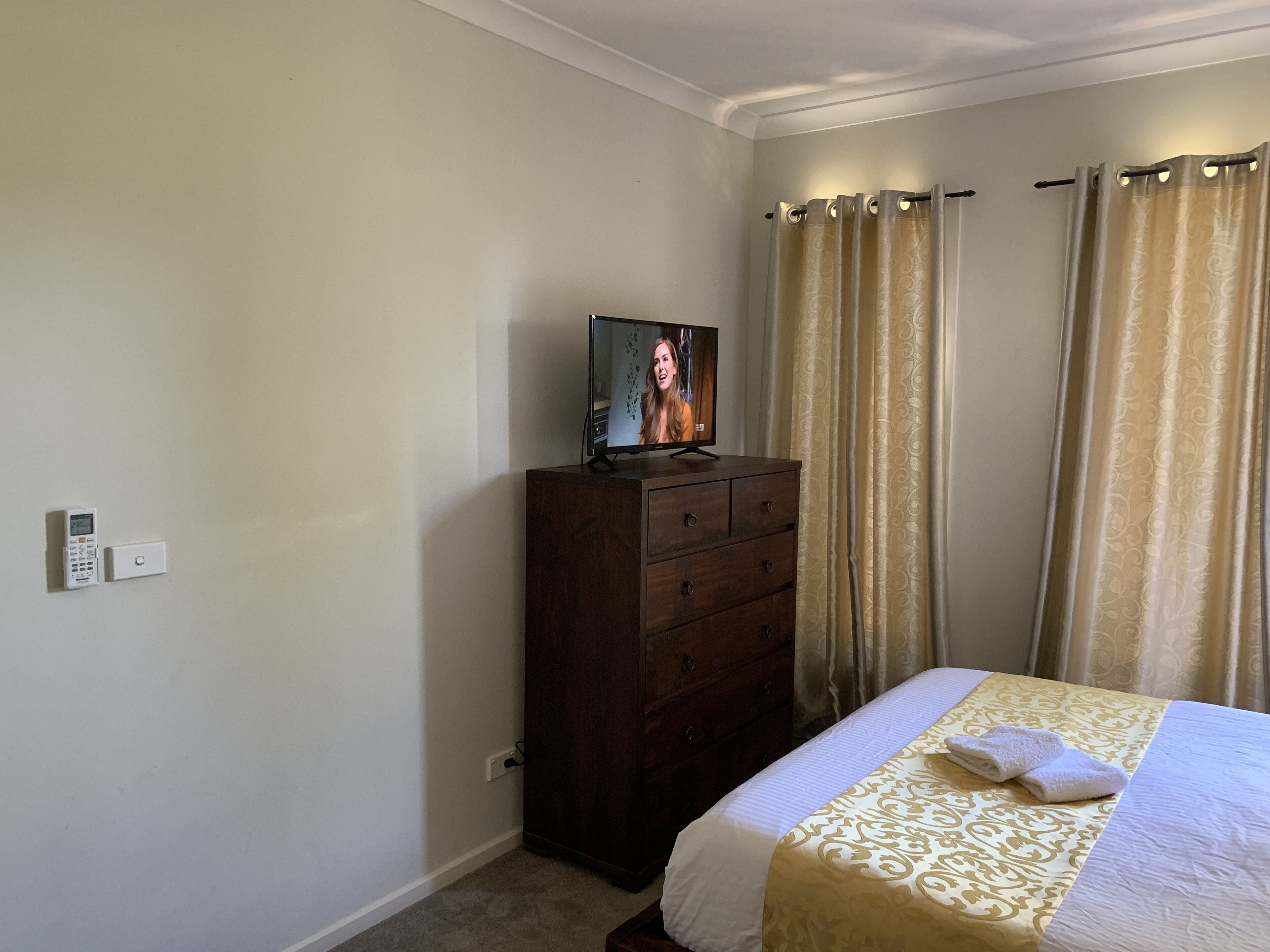 Una habitación de hotel con cama, cómoda, televisor y cortinas.
