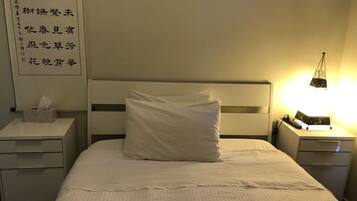 Ein Hotelzimmer mit einem ordentlich bezogenen Bett, einem Nachttisch mit Taschentuchbox und einem an der Wand befestigten Schild mit chinesischen Schriftzeichen.