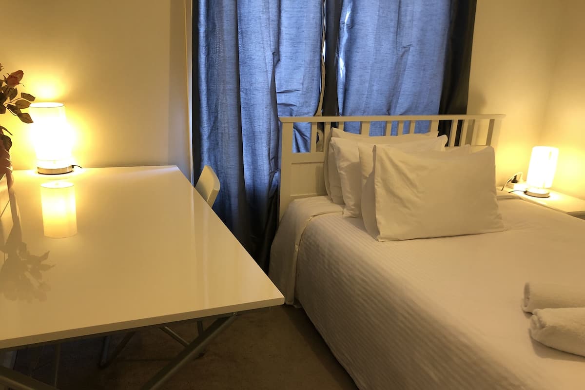 Une chambre d’hôtel avec un lit, une table de chevet, une lampe et une fenêtre avec des rideaux.