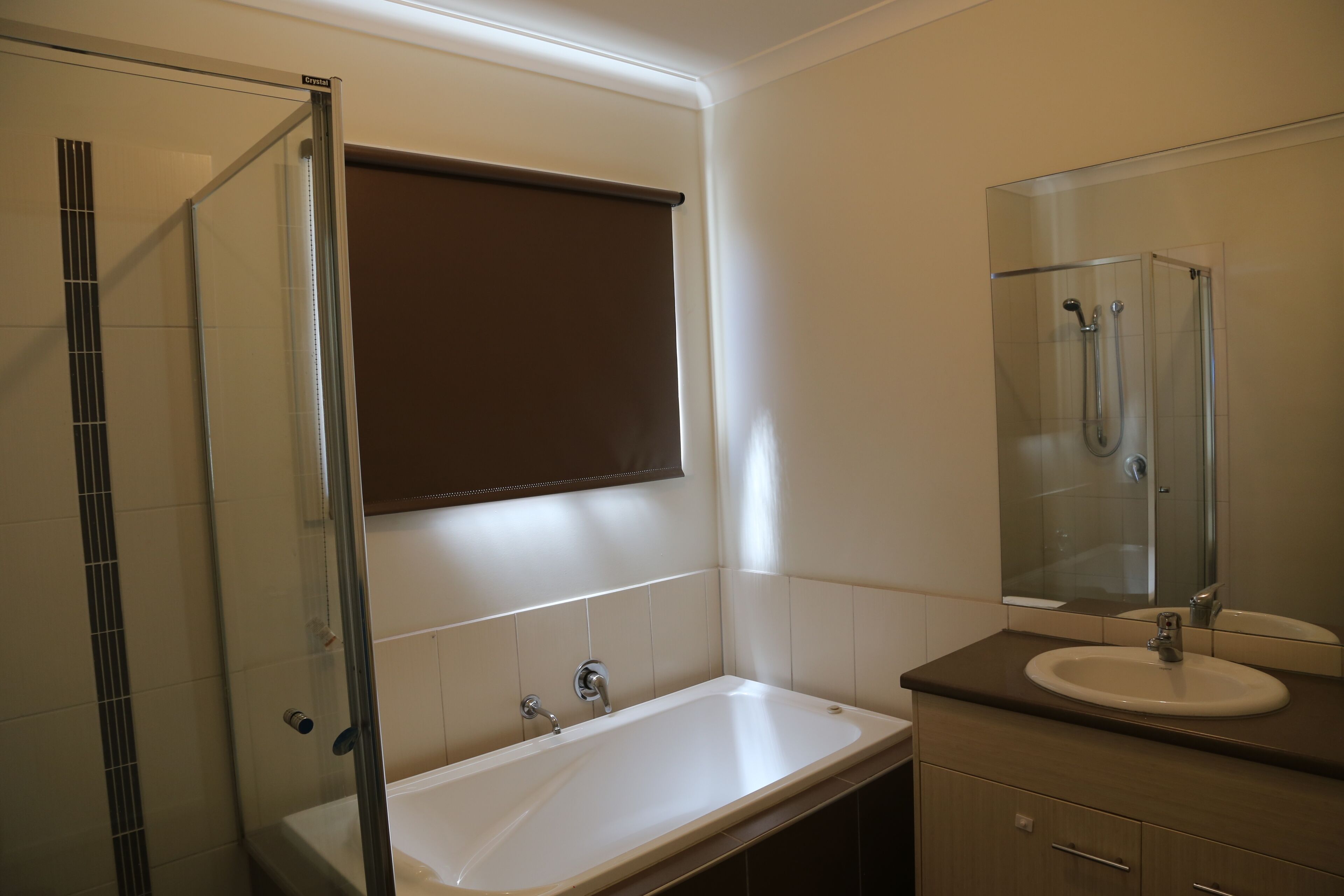 Een badkamer met een glazen douchecabine, een witte badkuip en een wastafel met spiegel.