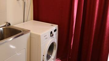 A compact laundry area with a washing machine, a sink, and a shower curtain.
