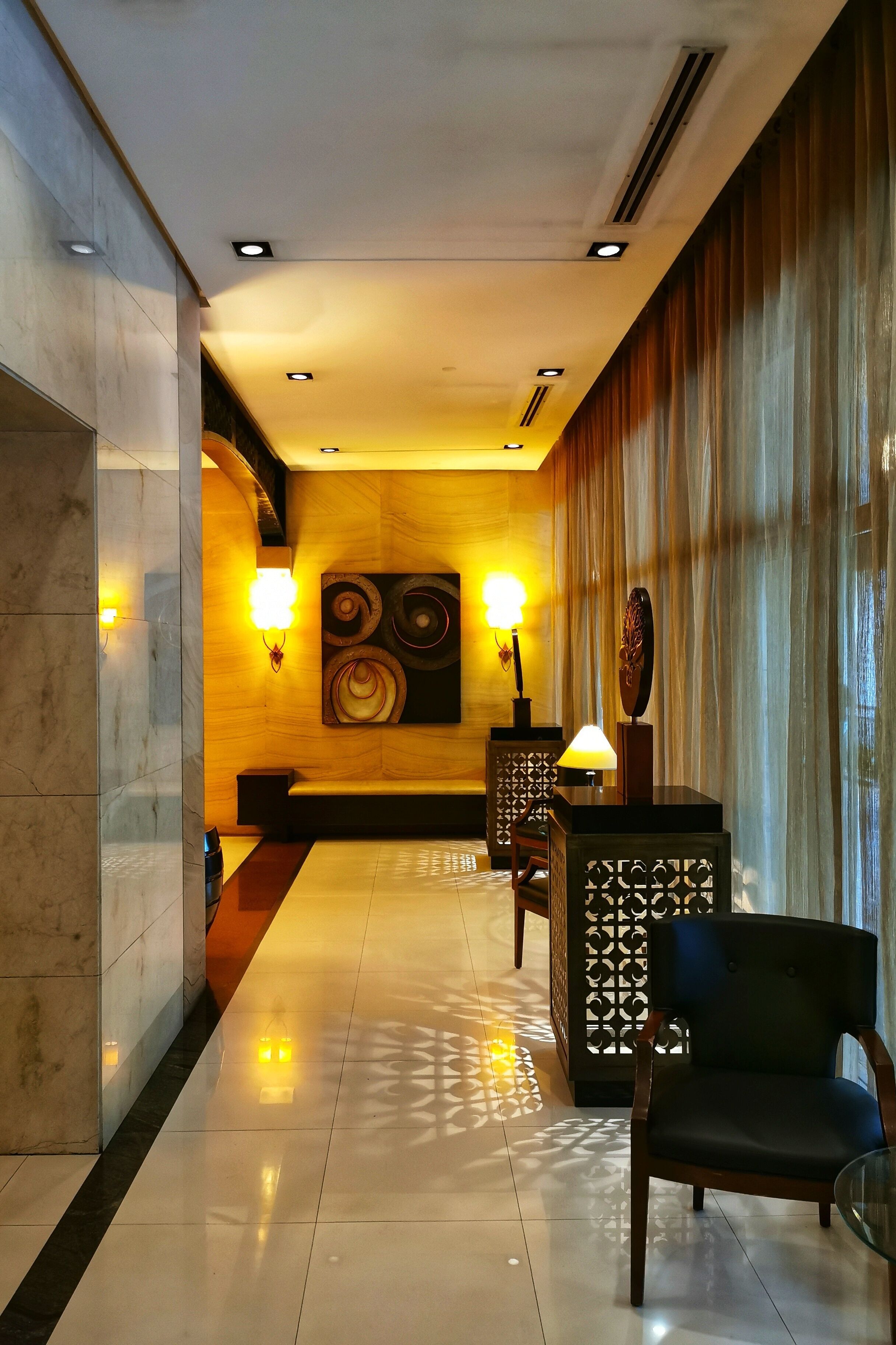 A hotel lobby with a marble reception desk, a black leather chair, and a decorative wall with wall sconces.