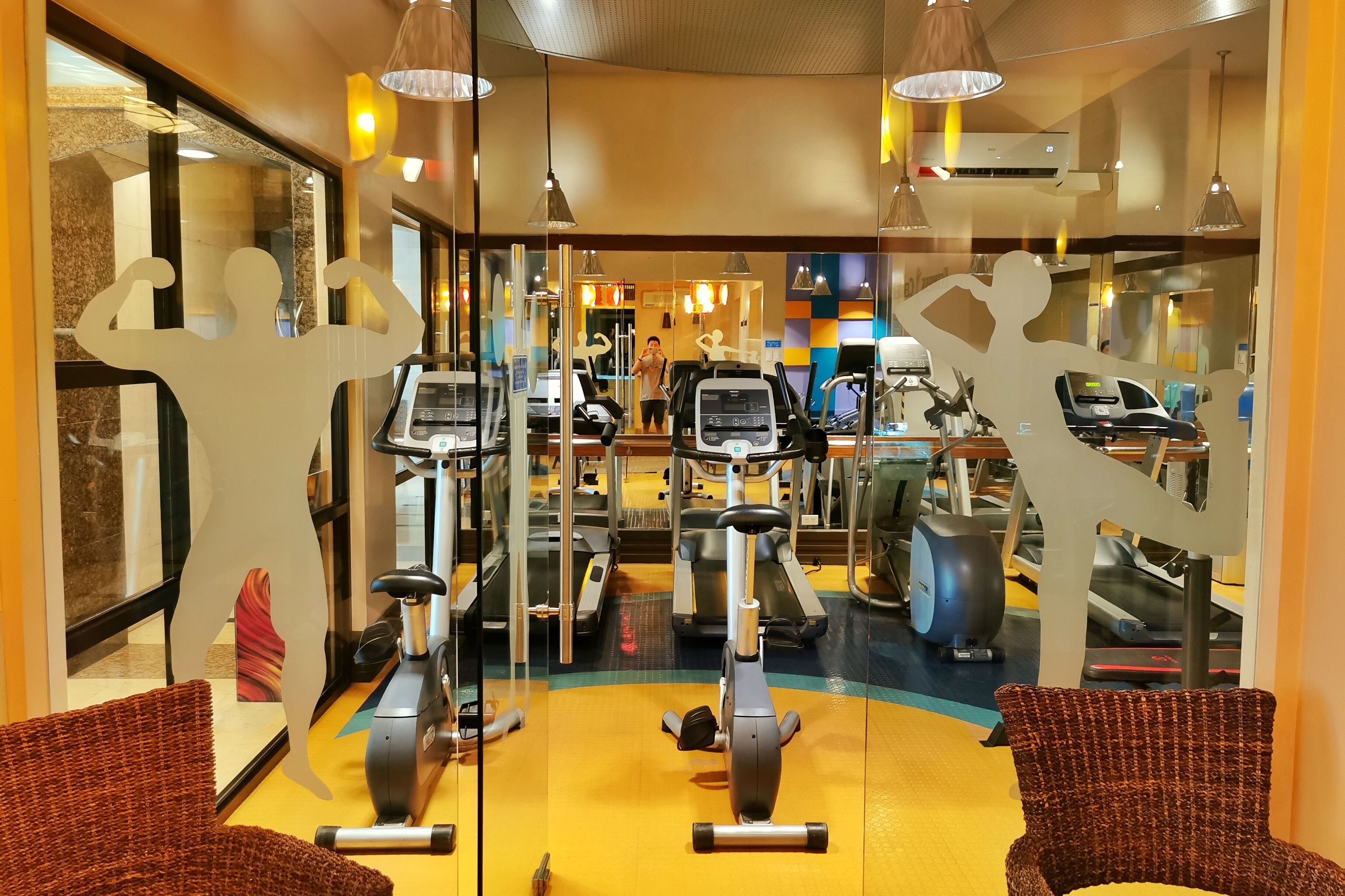 A gym with exercise equipment, mirrored walls, and a yellow floor.