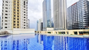 A swimming pool with a tiled surface and a view of tall buildings in the background. - Forbeswood Parklane (Taguig)
