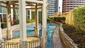 A covered outdoor swimming pool area with stone walls and a paved walkway. - Forbeswood Parklane (Taguig)