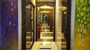 A modern hotel lobby with a marble floor, a glass elevator, and a colorful wall mural. - Forbeswood Parklane (Taguig)