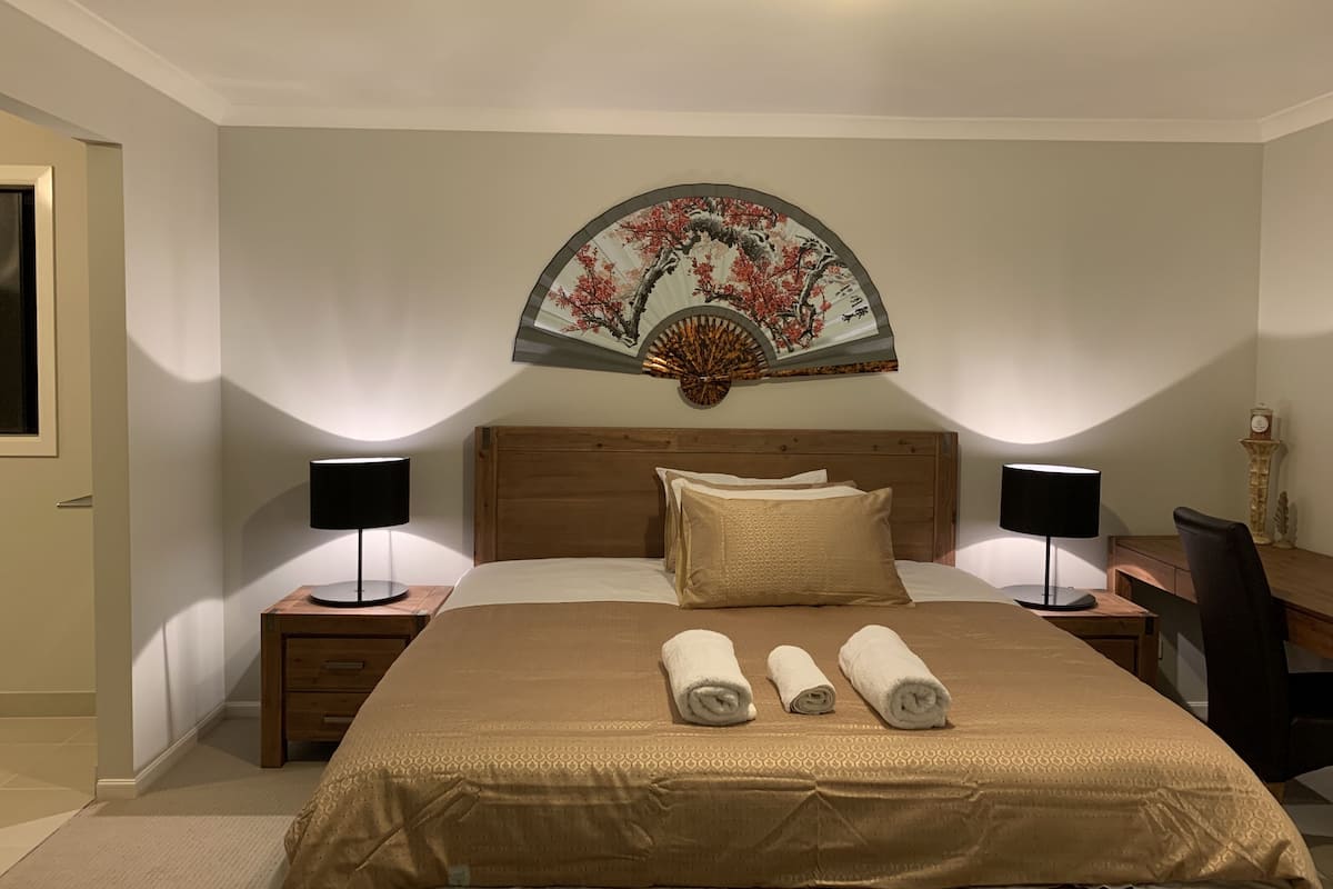 Une chambre d’hôtel avec un grand lit, deux tables de chevet avec des lampes, une tête de lit en bois et un éventail décoratif au-dessus du lit.