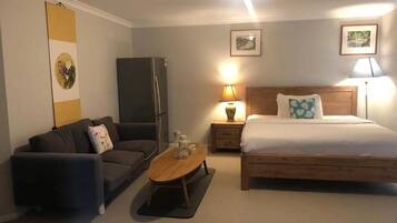 A bedroom with a bed, a sofa, a table, and a refrigerator.