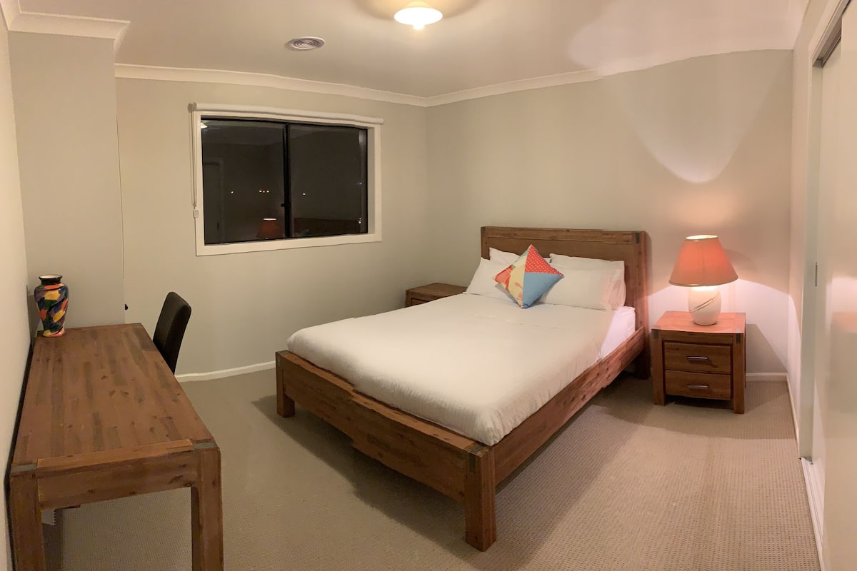 Une chambre à coucher avec un lit en bois, une table de chevet avec une lampe, un bureau en bois et une fenêtre.