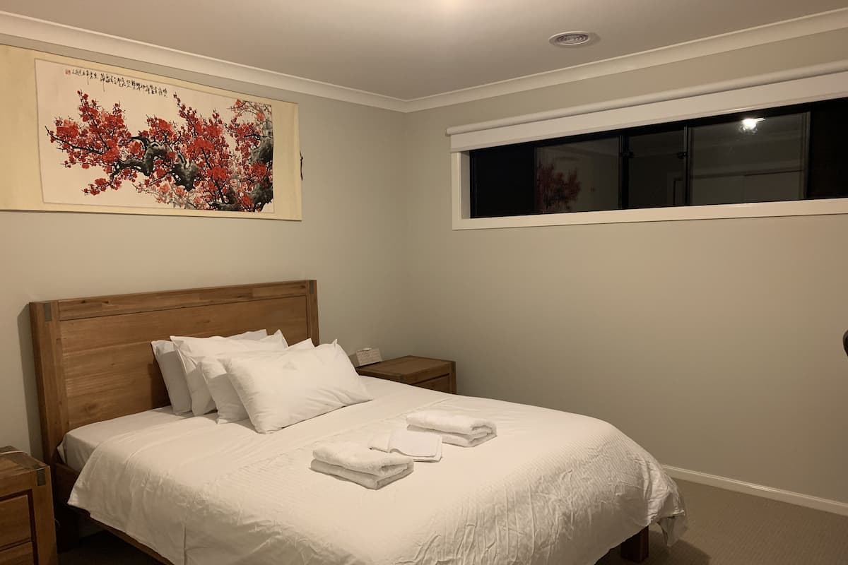 Un lit bien fait, avec du linge de lit et des serviettes blanches, une tête de lit en bois, une table de chevet avec une lampe et une fenêtre donnant sur le ciel nocturne.