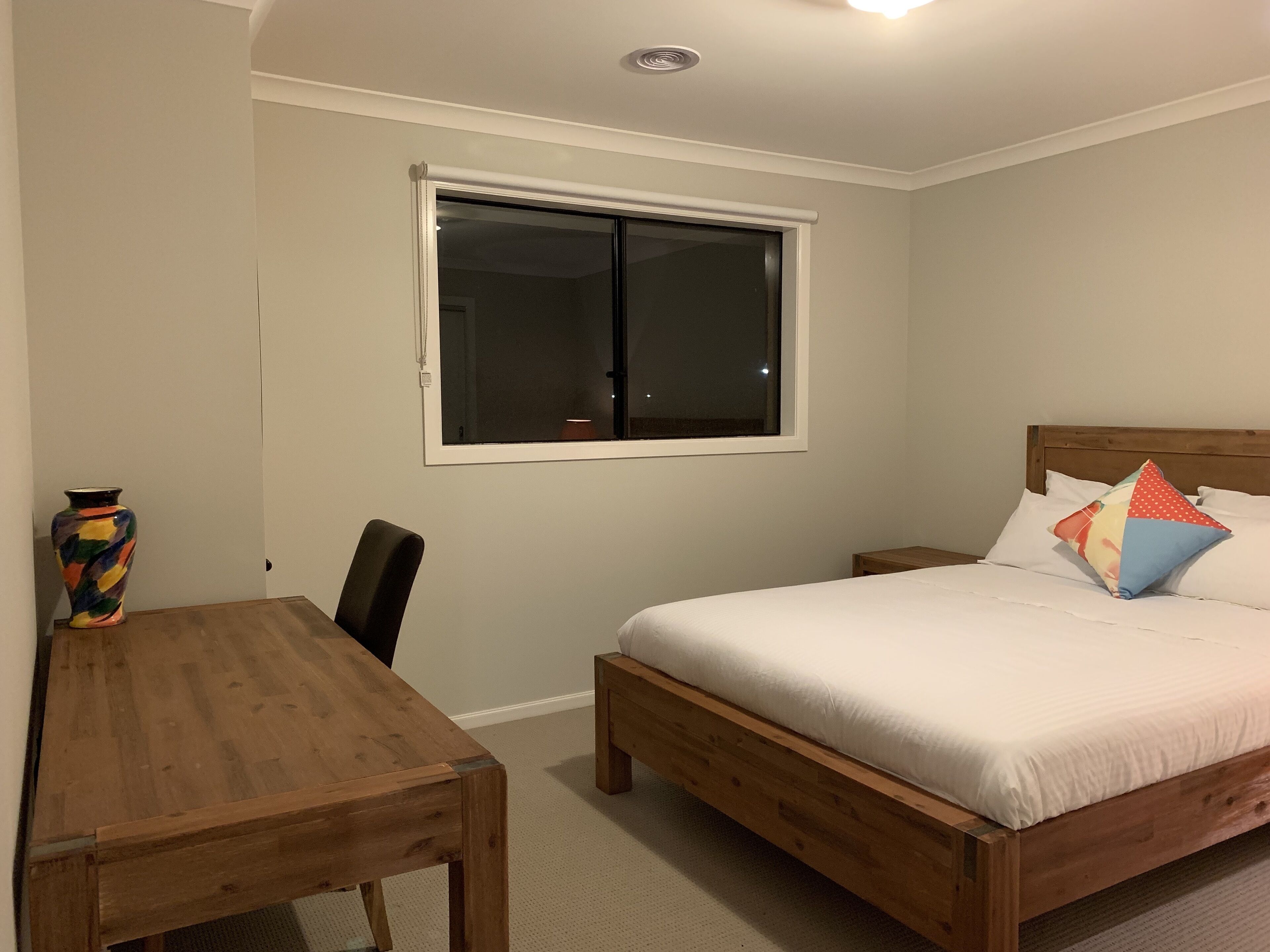 A bedroom with a wooden bed, a nightstand, a bedside table, a window, and a chair.