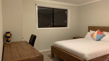 A bedroom with a wooden bed, a nightstand, a bedside table, a window, and a chair.