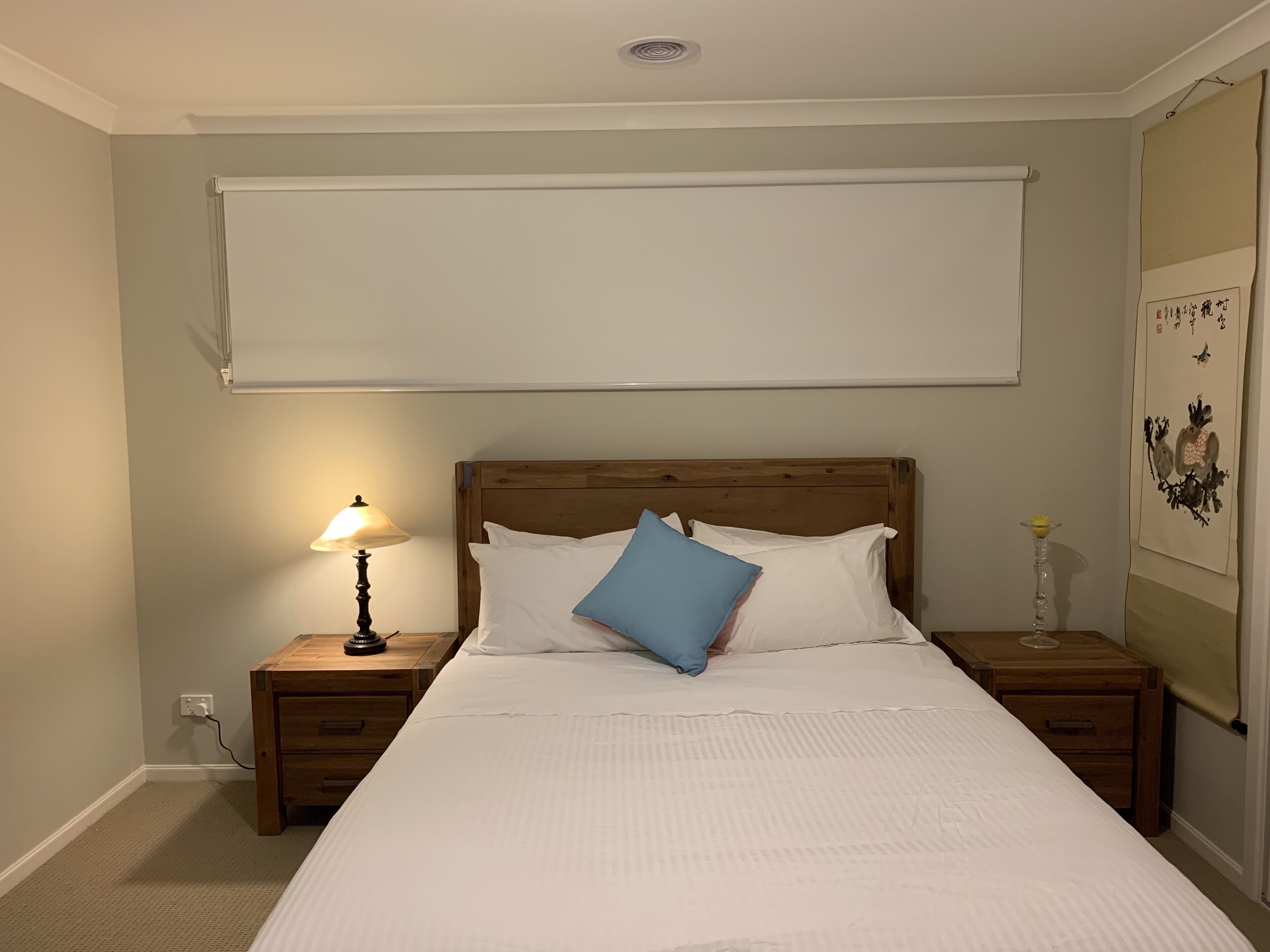 Cama bem arrumada com almofadas brancas e azuis, cabeceira de madeira e luminária de mesa.