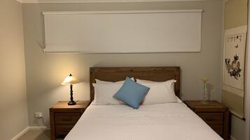 Cama bem arrumada com almofadas brancas e azuis, cabeceira de madeira e luminária de mesa.