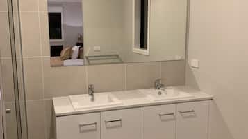 Ein modernes Badezimmer mit zwei Waschbecken, einem großen Spiegel und einer Duschkabine.