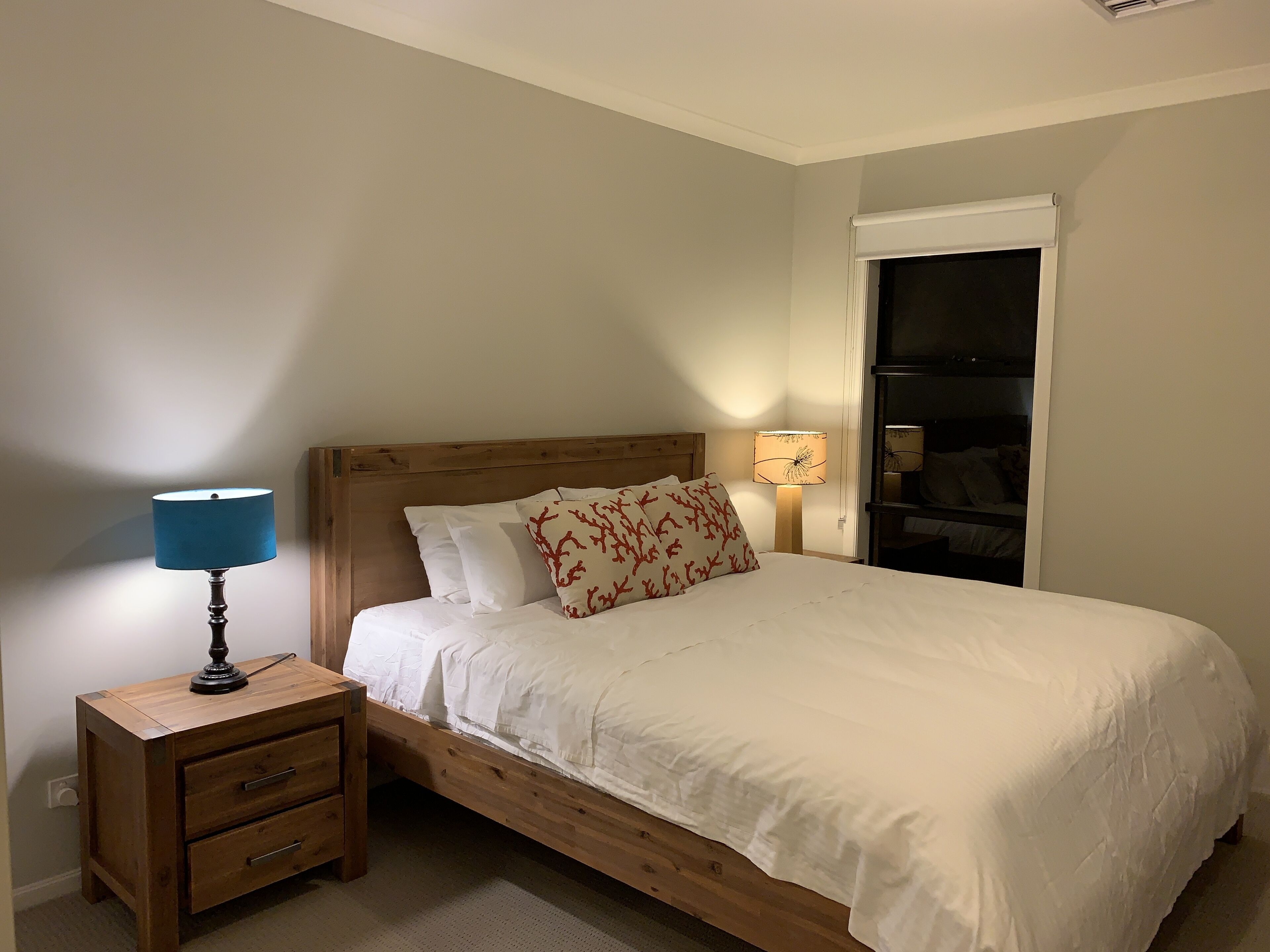 Un lit bien fait, avec une literie blanche et une tête de lit en bois, une table de chevet avec une lampe et une armoire avec un miroir.