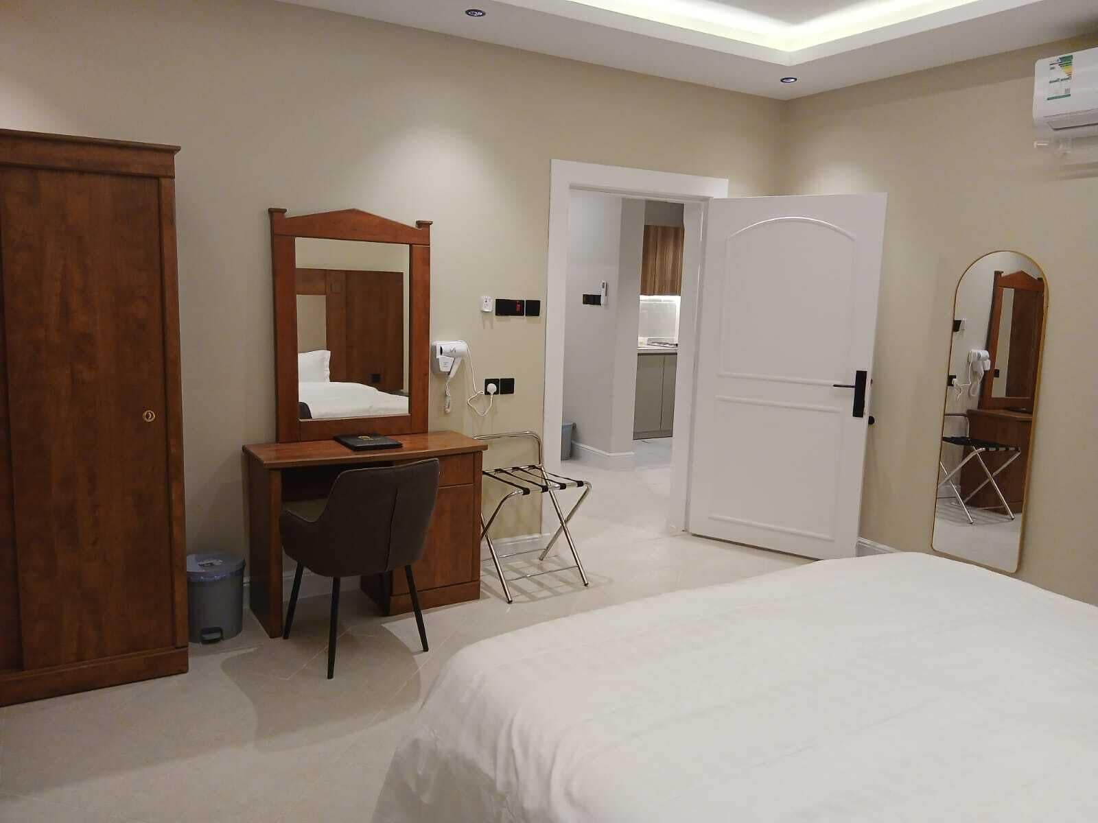Habitación de hotel con cama, escritorio con silla, espejo, armario y puerta que da a un baño.