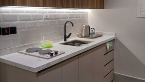 A modern kitchen with a white countertop, two sinks, a kettle, and wooden cabinets. - Raoum Inn Serviced Apartments-Shaqraa (Shaqra)