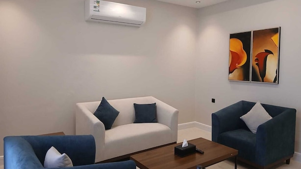 A modern room with a white sofa, two blue armchairs, a wooden coffee table, and abstract artwork on the wall. - Raoum Inn Serviced Apartments-Shaqraa (Shaqra)