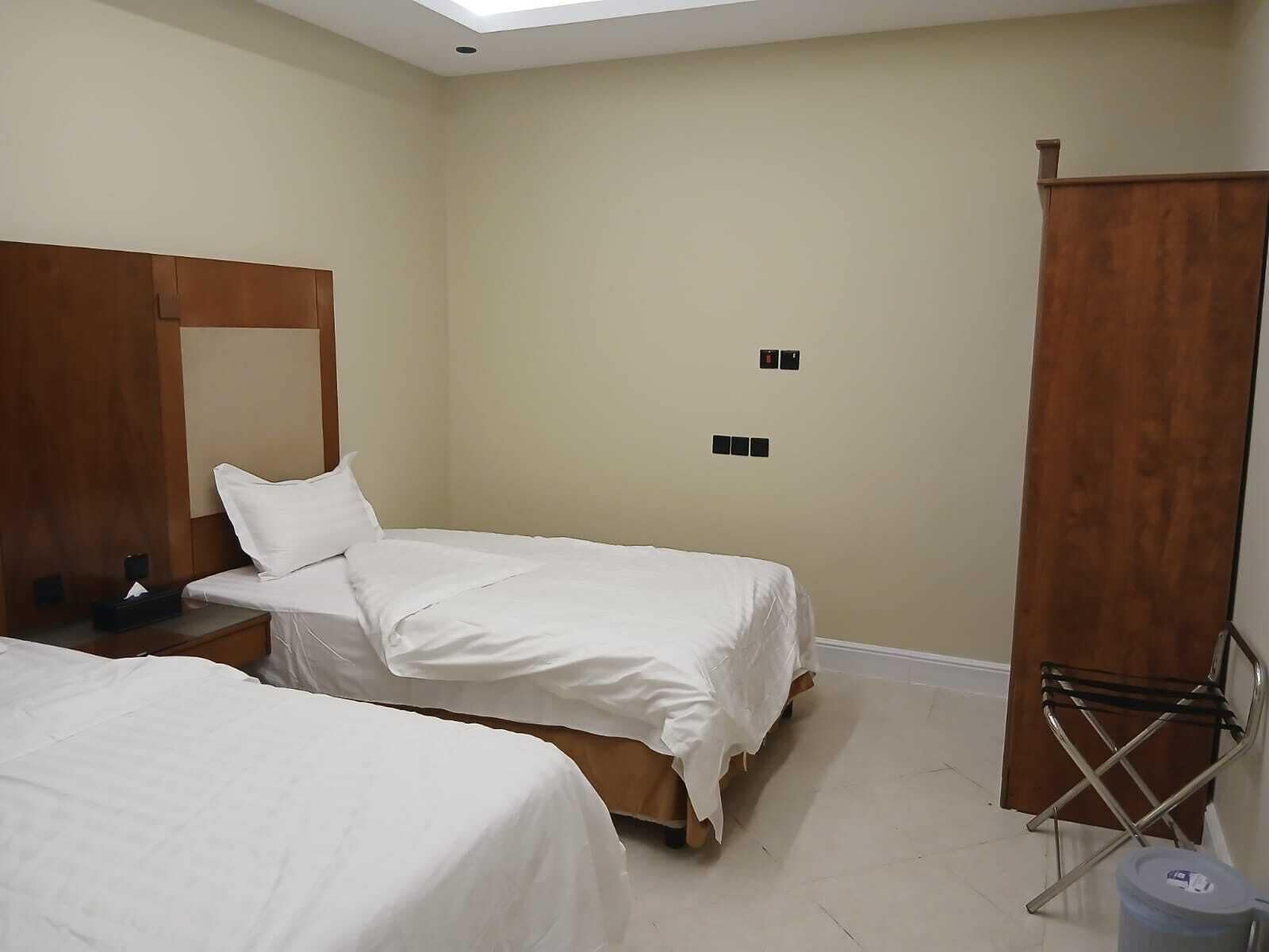 A hotel room with two single beds, a wooden wardrobe, a small table with a phone and tissues, and a ceiling light.