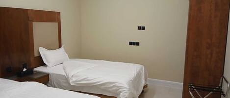 A hotel room with two single beds, a wooden wardrobe, a small table with a phone and tissues, and a ceiling light.