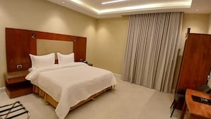 A hotel room with a large bed, a wooden headboard, a bedside table, a desk, and a chair. - Raoum Inn Serviced Apartments-Shaqraa (Shaqra)