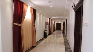 A hotel corridor with a marble floor, red and beige curtains, and a modern ceiling with recessed lighting. - Raoum Inn Serviced Apartments-Majmaa (Al Majmaah)
