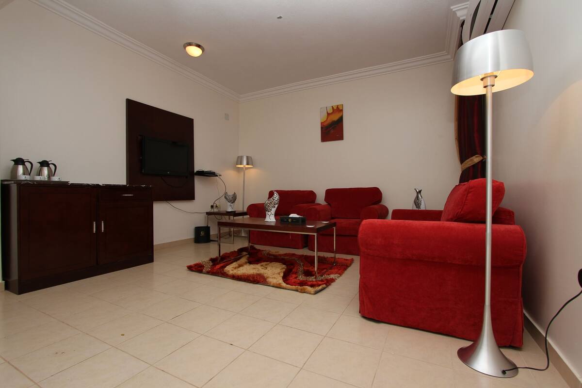 A living room with a red sofa, a coffee table, a floor lamp, and a TV mounted on the wall.