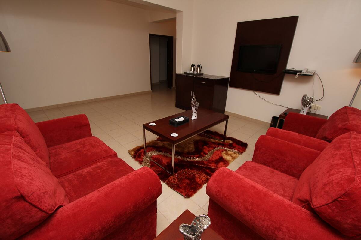 A living room with red sofas, a coffee table, and a TV mounted on the wall.