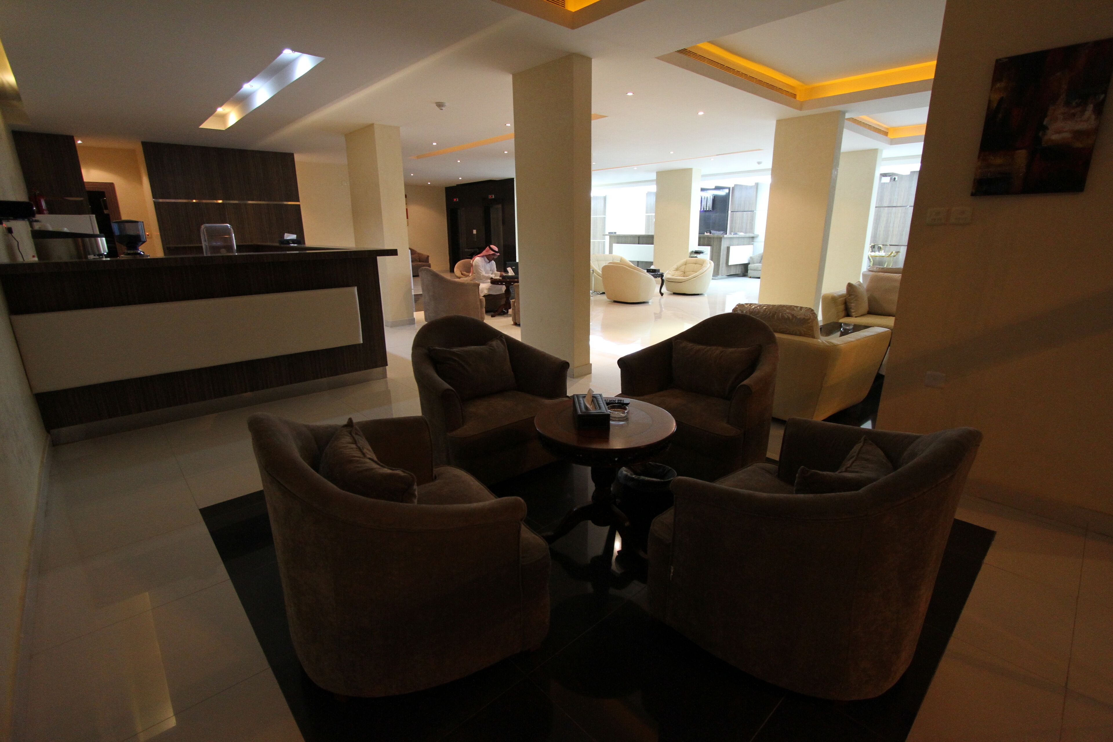 A modern hotel lobby with a reception desk, seating area with sofas, and a large open space with a dining area.