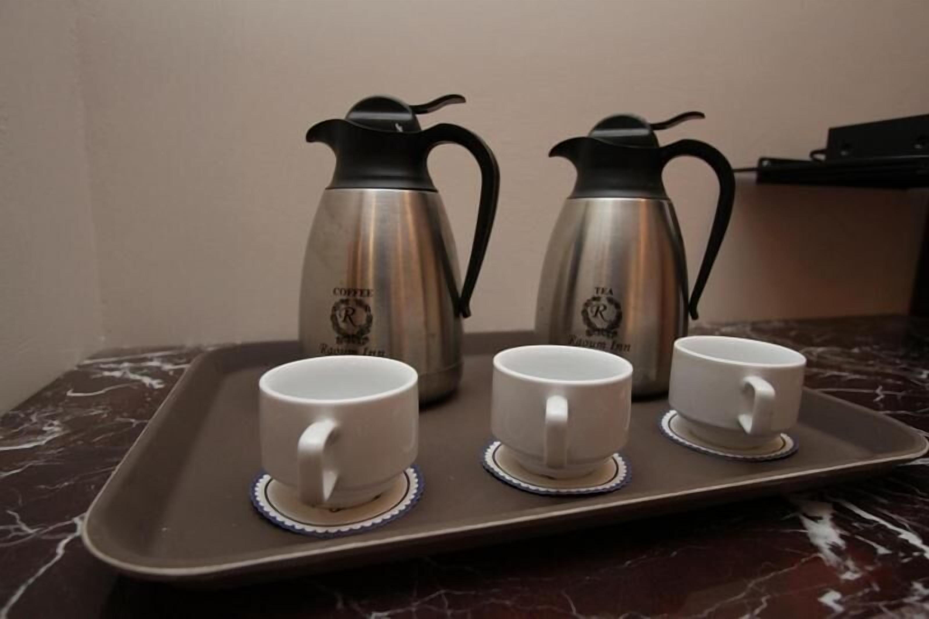 Un plateau contenant deux cafetières en acier inoxydable et trois tasses blanches avec leurs soucoupes, posé sur un comptoir en marbre.