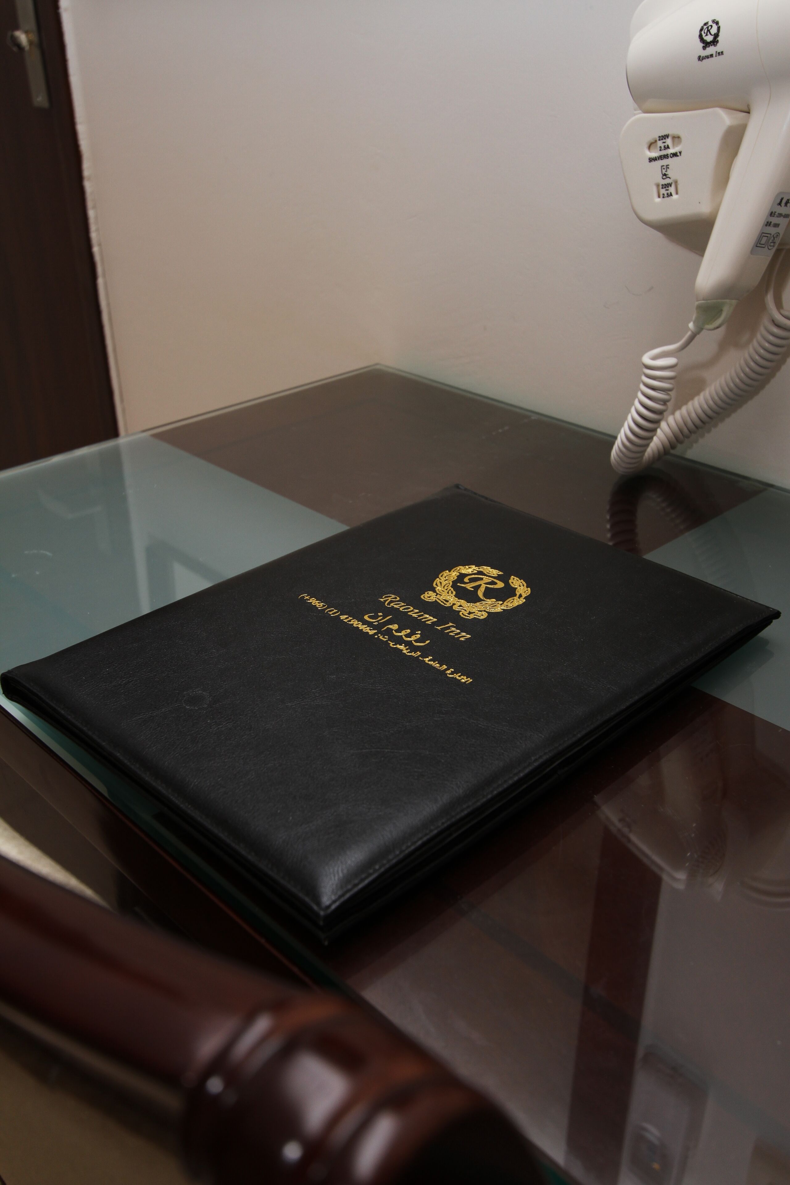 Ein schwarzes, ledergebundenes Buch mit dem Titel „Kleiner Fünf“ auf einem Glastisch, neben einem Telefon und einem hölzernen Gegenstand.