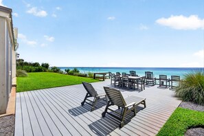 A wooden deck with outdoor furniture overlooking a clear blue sea.