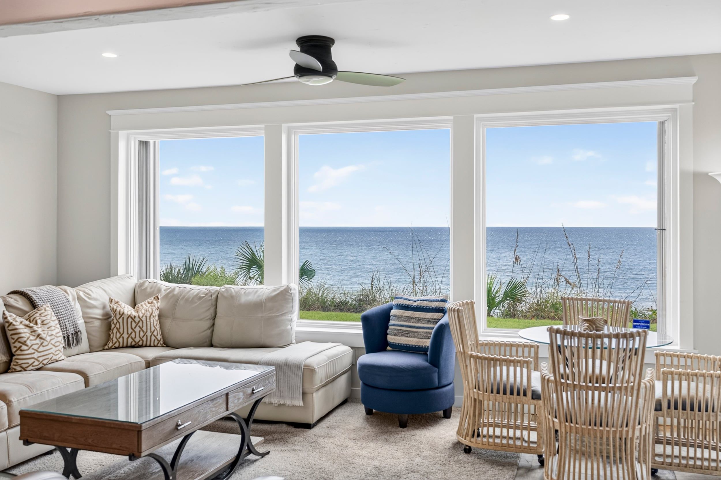 A living room with a large window overlooking the sea, a sofa, a coffee table, and a chair.