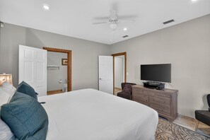 A hotel room with a large bed, a television, a dresser, and a ceiling fan.