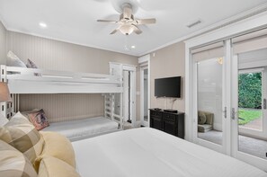 A bedroom with a bunk bed, a flat-screen TV, a desk with a chair, and a sliding glass door leading to a garden.