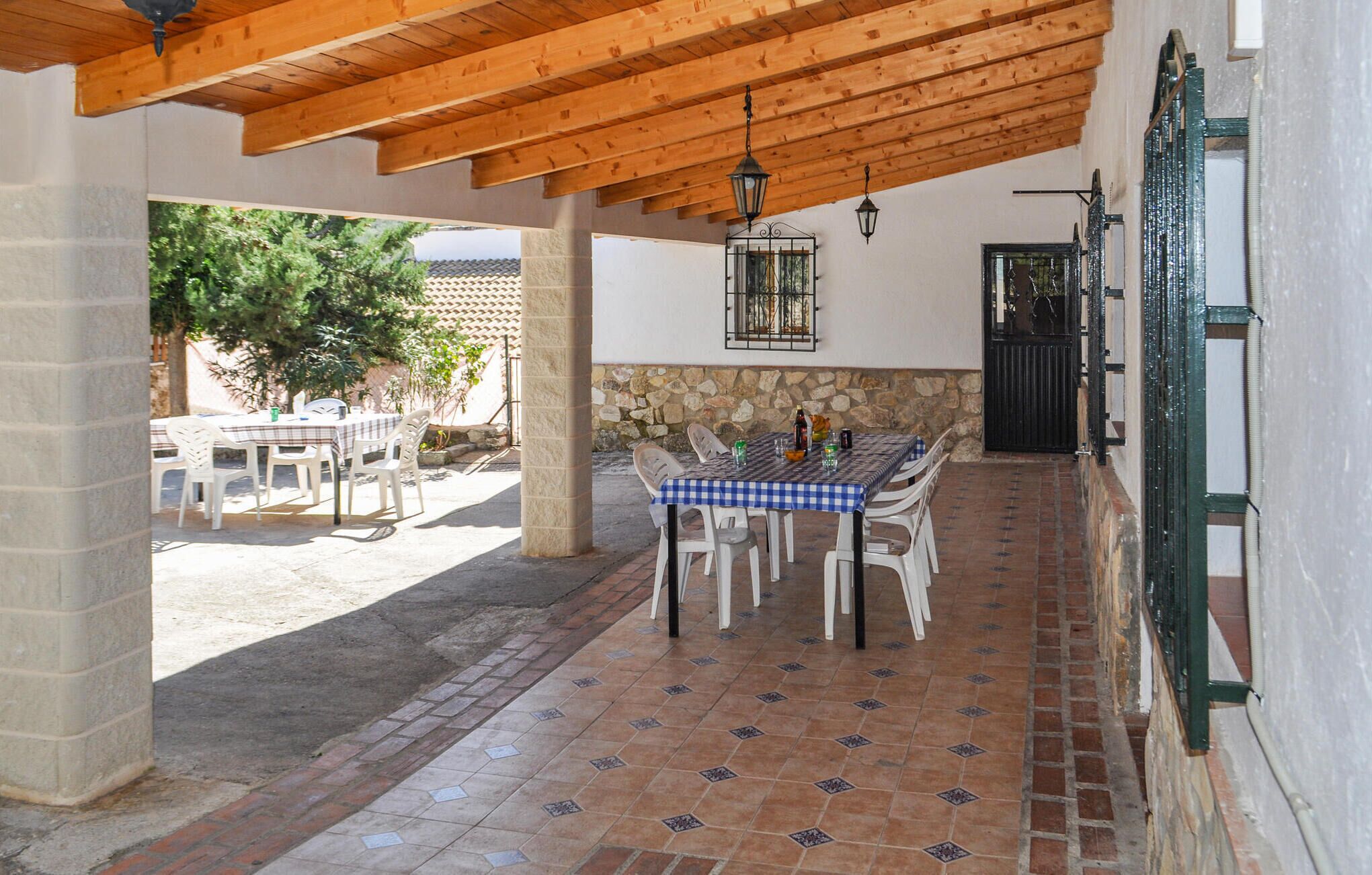 An outdoor patio area with a checkered tablecloth, white chairs, and a stone wall.