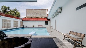 A swimming pool with a red-tiled roof, a bench, and a wall-mounted air conditioning unit. - Hotel Sumaryo (Yogyakarta)